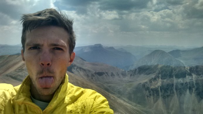 A defiant hiker sticking his tongue out on the summit of Redcloud Peak with Sunshine Peak in the background