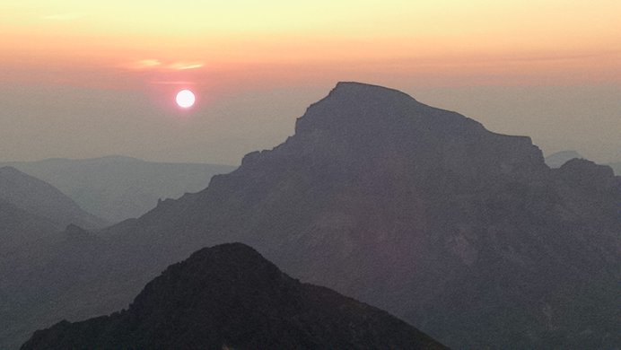 The silhouette of Wetterhorn Peak with a red-orange sun rising behind