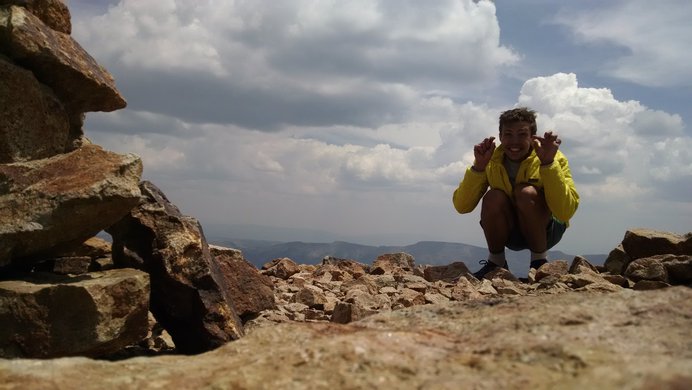 I crouch for a self-timer photo on Sunshine Peak as gentle clouds roll in