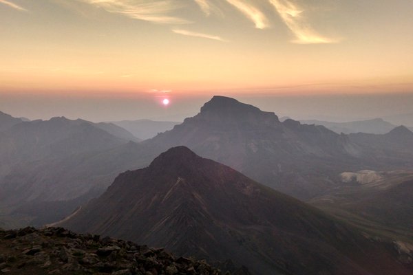 The sun begins to rise into a hazy sky behind Uncompahgre Peak, seen from Wetterhorn Peak